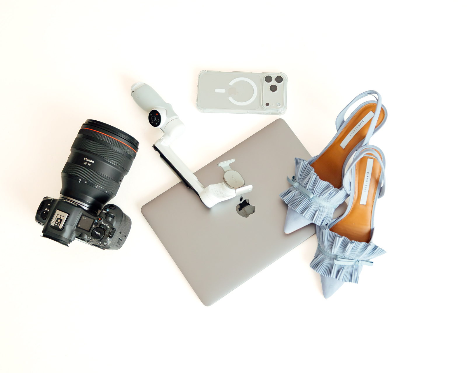 Flatlay of a camera, laptop, phone, gimbal and blue heels